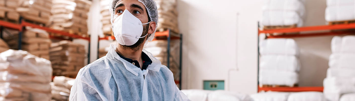 A worker wearing a mask takes inventory in a warehouse.