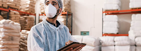 A worker wearing a mask takes inventory in a warehouse.