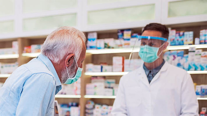 A pharmacist assists customers, all are wearing face coverings.