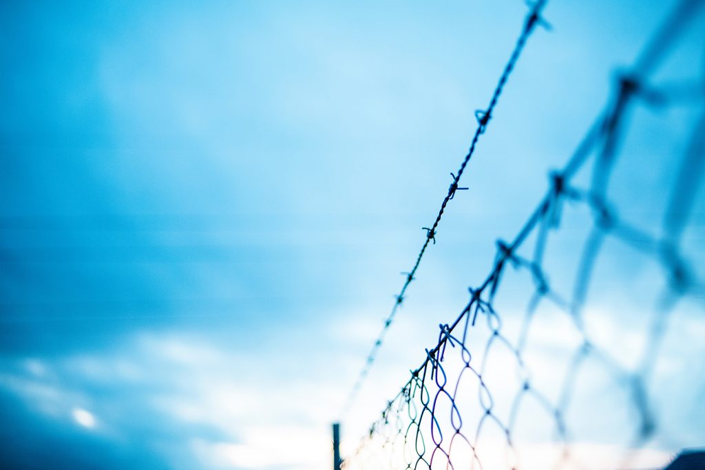 A fence topped with barbed wire under a wispy blue sky