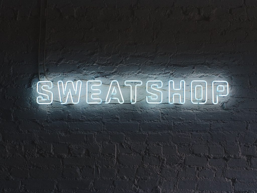 A neon sign on a wall reads 'sweatshop'