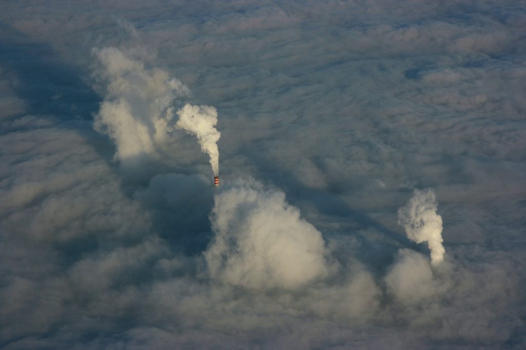 Chimneys, poking through clouds viewed from above, emit their own troublesome vapours