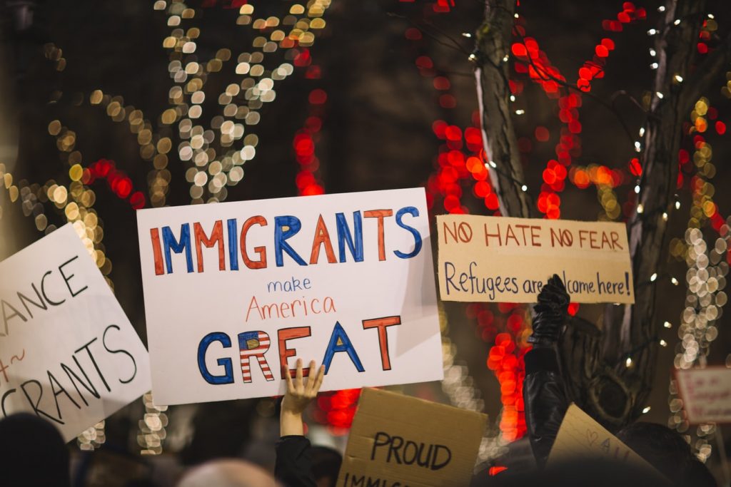 Hands of demonstrators holding signs, one of which reads 'immigrants make America great'