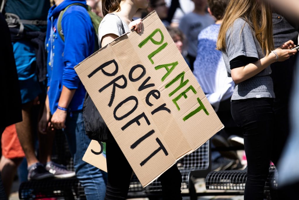 A protester carries a cardboard sign saying 'Planet over profit'