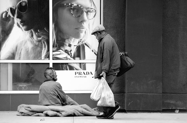 A homeless man sits outside a luxury shop
