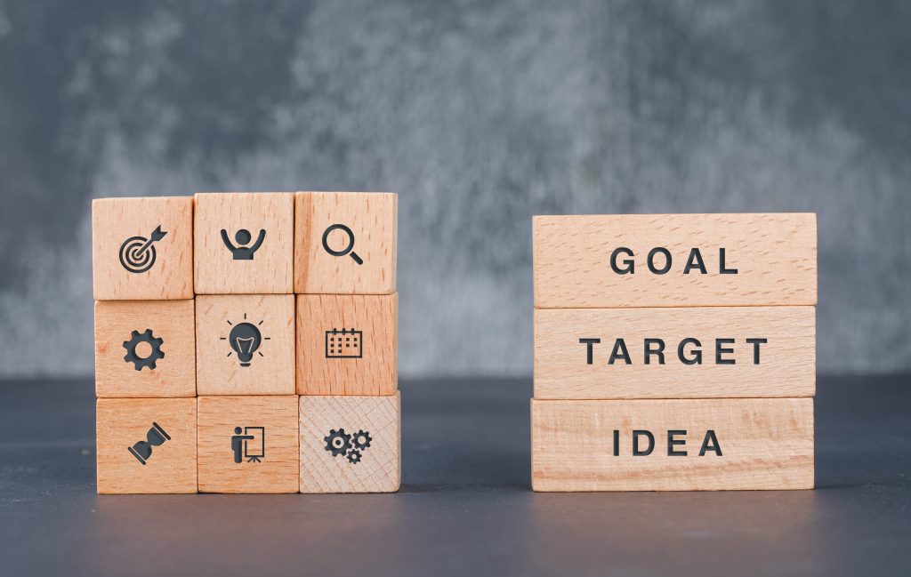 photo of square wooden blocks with icons stack on top of each other and 3 rectangular wooden blocks with word "goal", "target" and "idea" stacked on top of each other