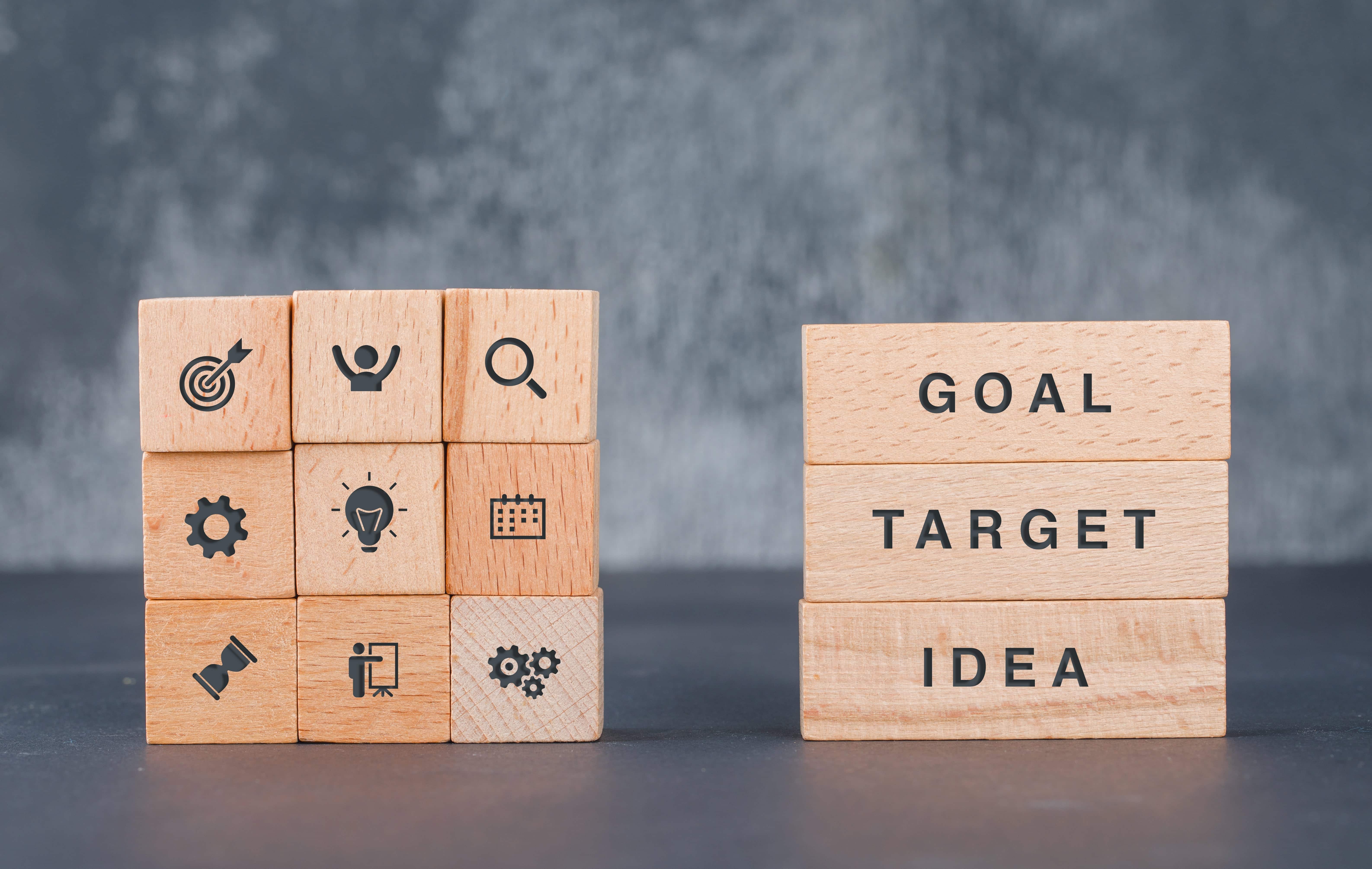 photo of square wooden blocks with icons stack on top of each other and 3 rectangular wooden blocks with word "goal", "target" and "idea" stacked on top of each other