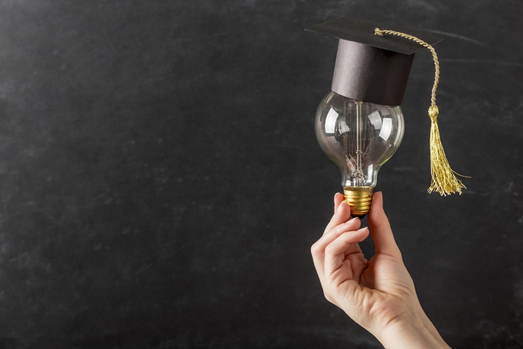 Hand holding light bulb with graduation cap, on a black background