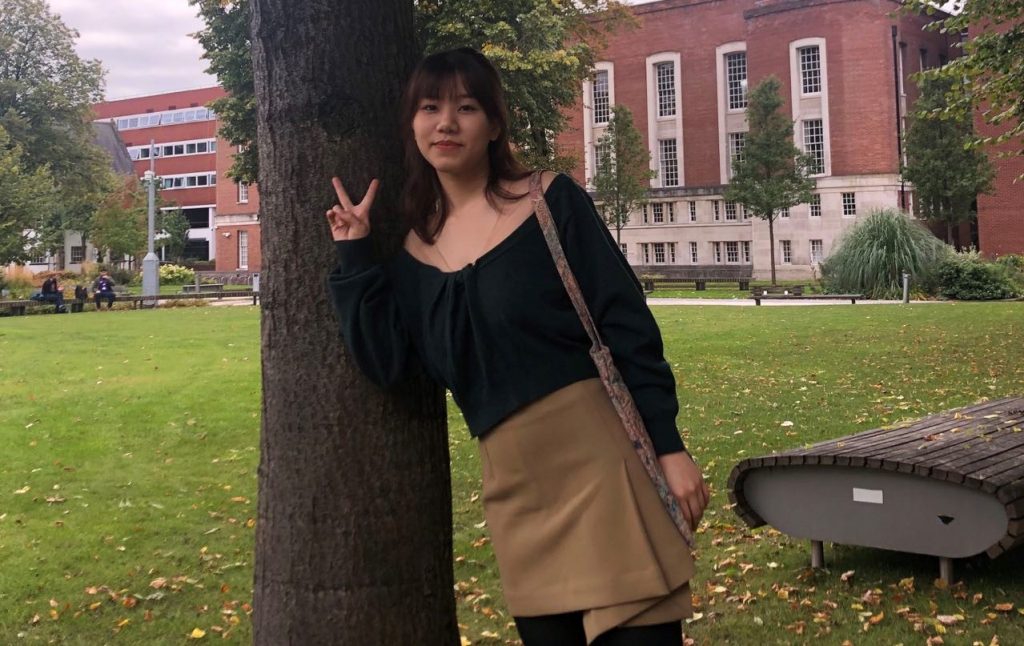 Girl doing a peace sign in front of a tree on campus