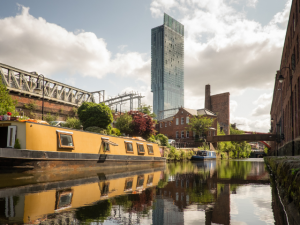 Manchester city buildings, house boat, canal surrounded by greenery 
