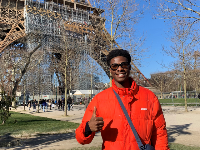 Man smiling standing with his thumbs up in front of the Eiffel Tower