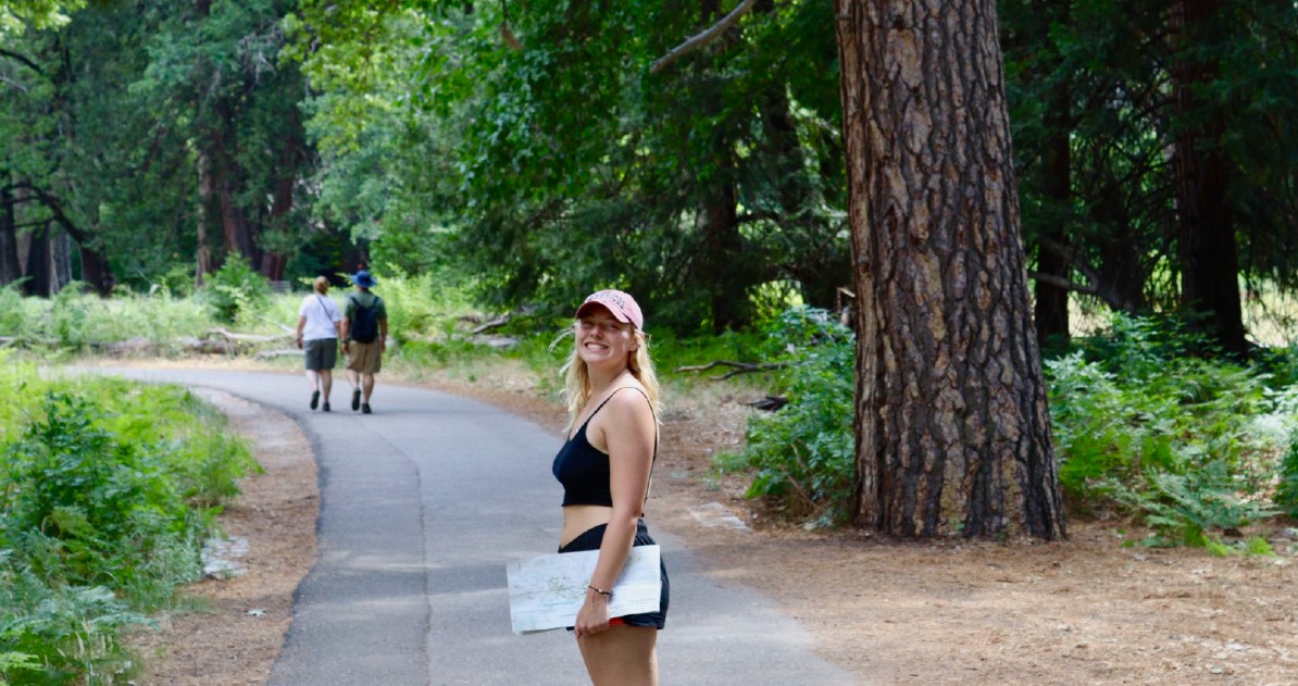 Female student stands in a park smiling