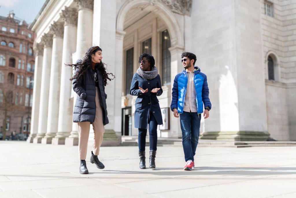 Three students walk through The University of Manchester