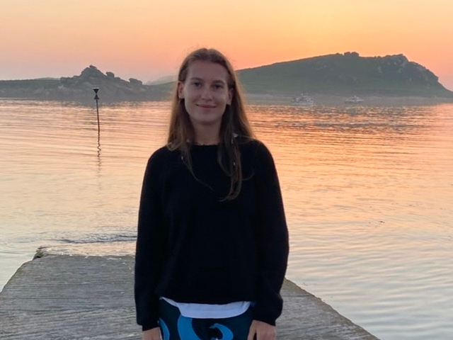 Student stood in front of a lake at sunset