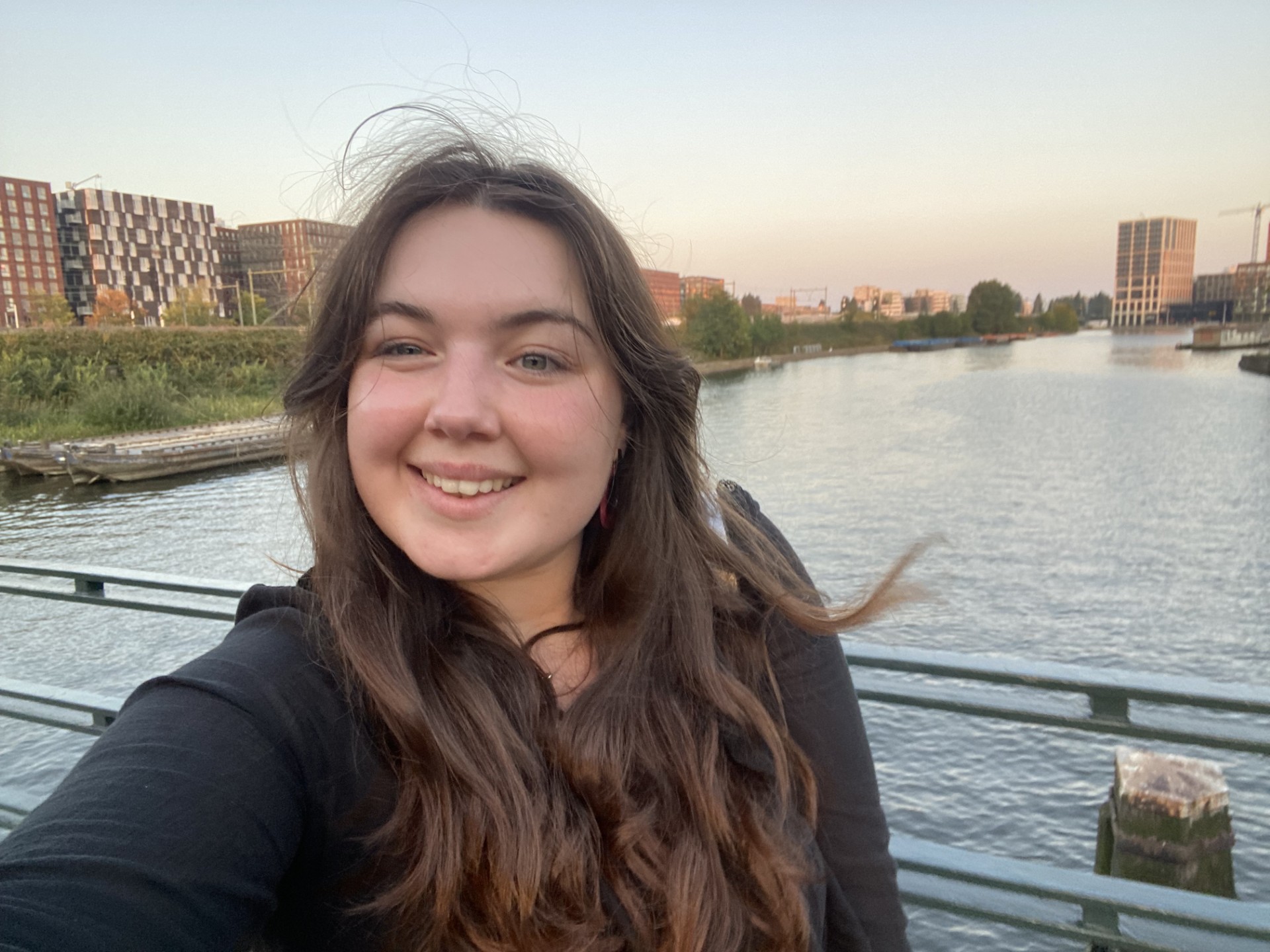 Jess Author Photo A young woman stands on a bridge, with a wide river and cityscape in the backdrop