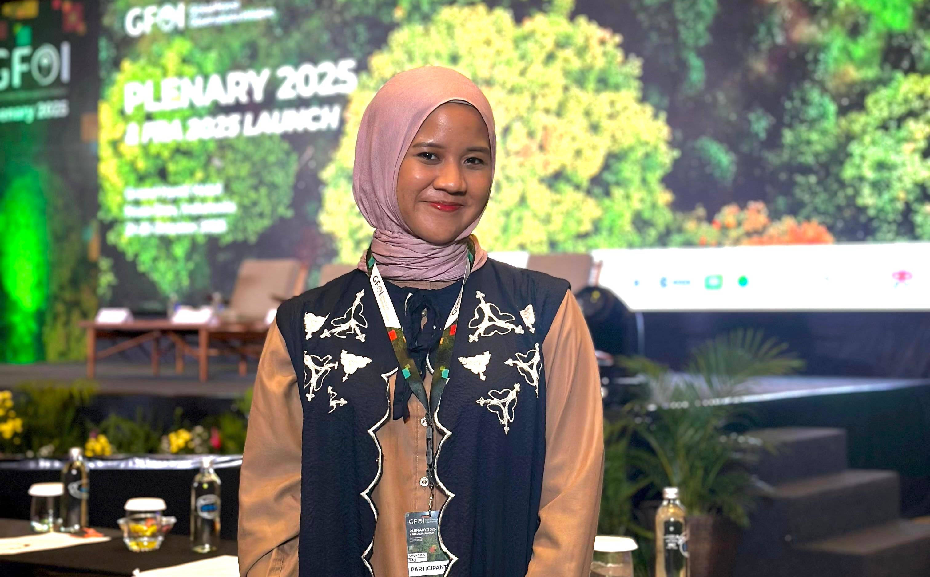 alumniphoto-SESIA 3024×1874 Sesia stands in front of a projection of a green forest, about to present her work.
