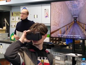 Student looking through VR headset while academic narrates the virtual tour