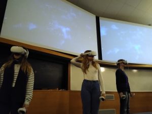 Three students using VR headsets in front of lecture screen