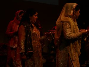 Women on stage preparing for the Mehndi ceremony, which consists of traditional singing and dancing in South Asian culture, and is common before the wedding day. The Mehndi ceremony represents the bond of matrimony and signifies the love and affection between the couple and their families.