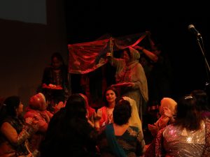 Women on stage reenacting a scene of a bride entering the room