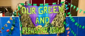 Walking banner contributed to St George's Day Parade 2022. The banner says Our Green and Pleasant Land and has shapes of mountains and a painted blue and purple sky on it.