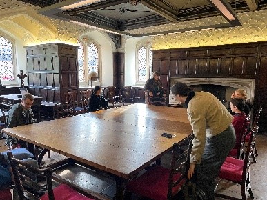 Beautiful old room with wood panelling, and a large table in the centre. People are seated around the table.